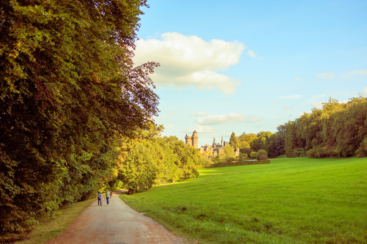 A path across a meadow toward a turreted building, two people walking