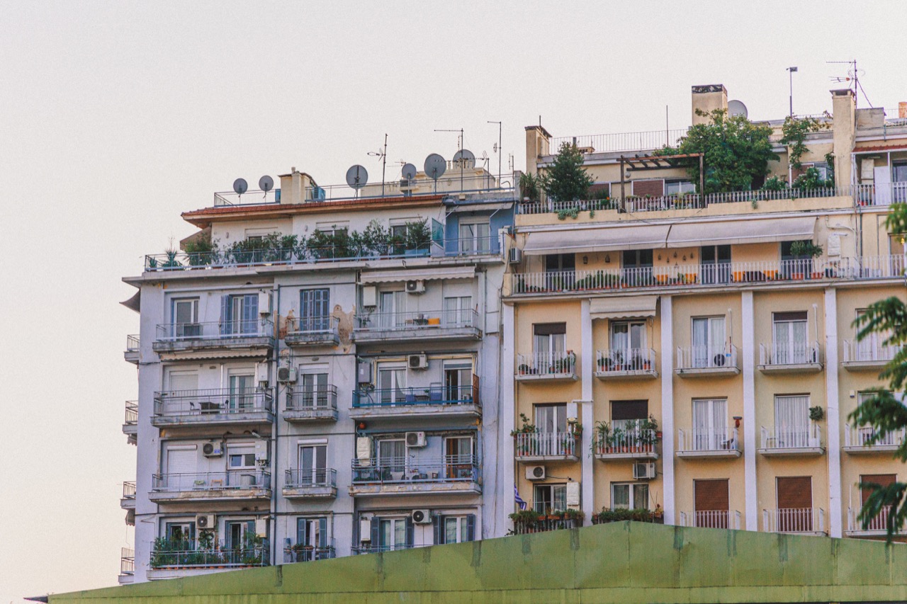 An apartment block with plant-filled balconies against a pale sky